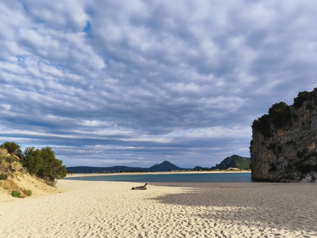 Sandy shore of Voidokilia Beach with turquoise waters and a rocky headland
